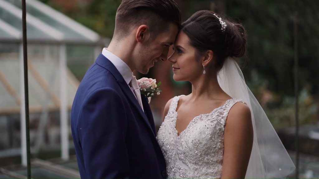 Bride and Groom resting their foreheads together by green house