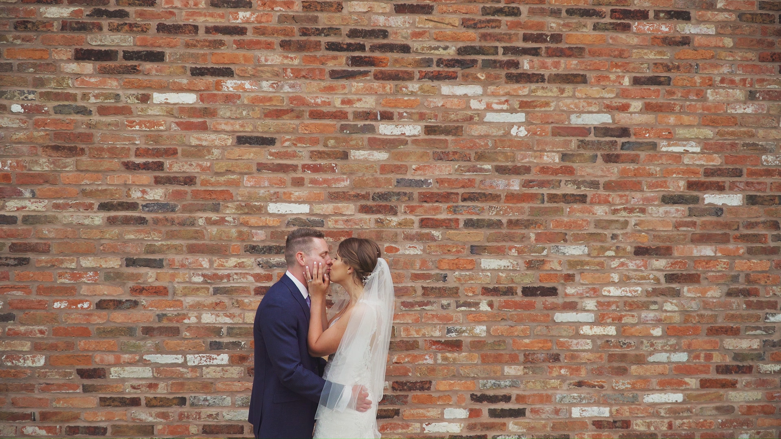 Bride and Groom kissing in front of a large brick wall