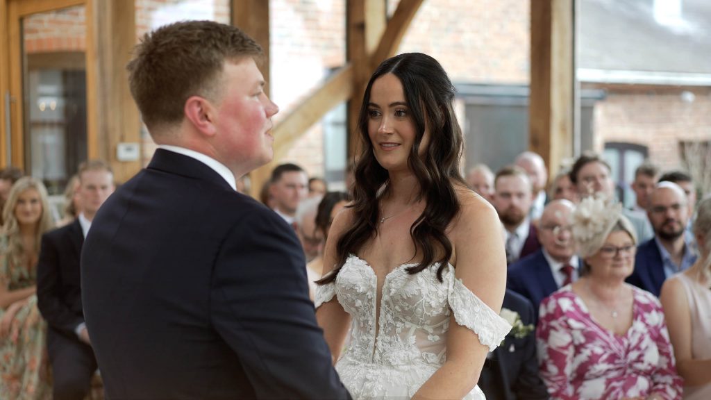 A couple during their wedding ceremony taking place in the glass barn at Swancar Farm