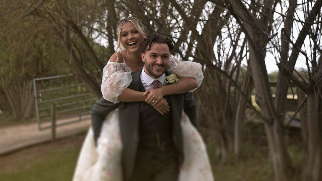 Bride and groom piggy back outside Swancar Farm