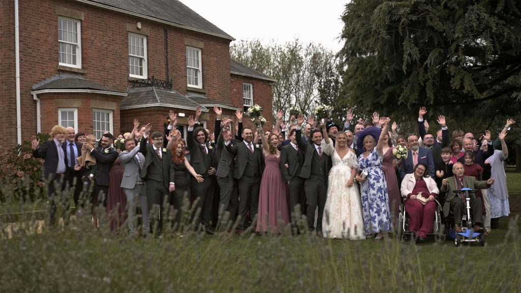 Whole wedding party cheering in a big group outside Swancar Farm Country House