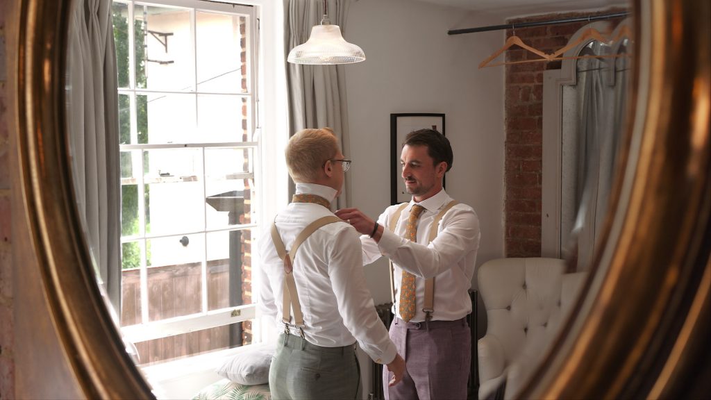 Grooms together helping each other get ready during the wedding morning