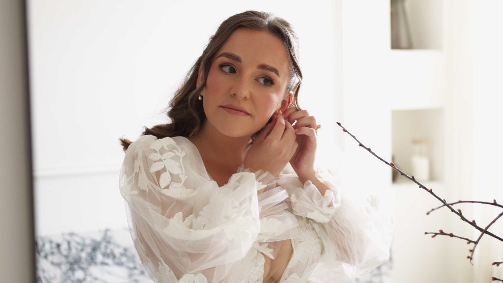 Bride getting ready in bridal suite, putting in her earrings while looking in a mirror